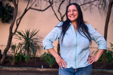 Güzel, gülümseyen, karizmatik ve neşeli bir Latin yöneticinin portresi, doğal bir parkta tutum ve feminizmle poz veriyor. İyilik, yaşlılık, güzellik..                               