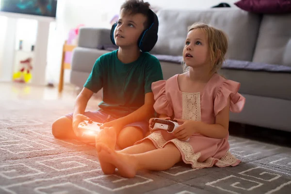 Petit frère et sœur jouant à des jeux vidéo allongés sur le canapé — Photo