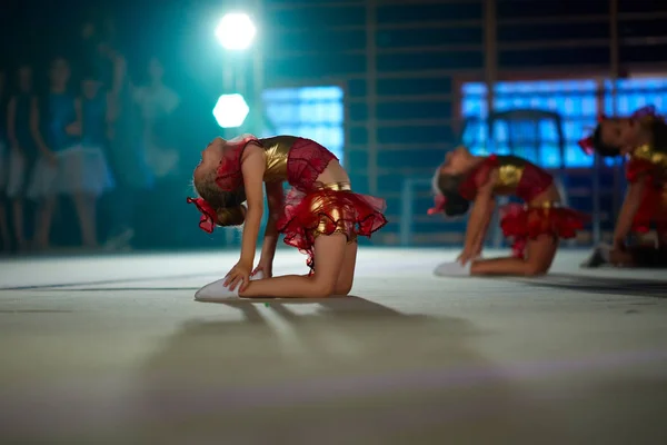Little gymnasts do exercises and are flexible, sitting on the floor on stage
