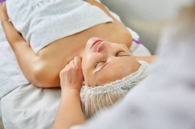 doğal yüz maskesi yüzünde uygulanırken masaj masanın üzerinde yatan güzel genç kadın