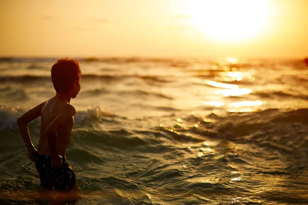 そこの方法の波と夕日に向かって外を見て少年. — ストック写真