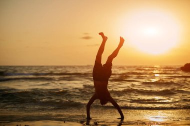 Çocuk günbatımı sırasında denizde alışılmadık bir sportif poz