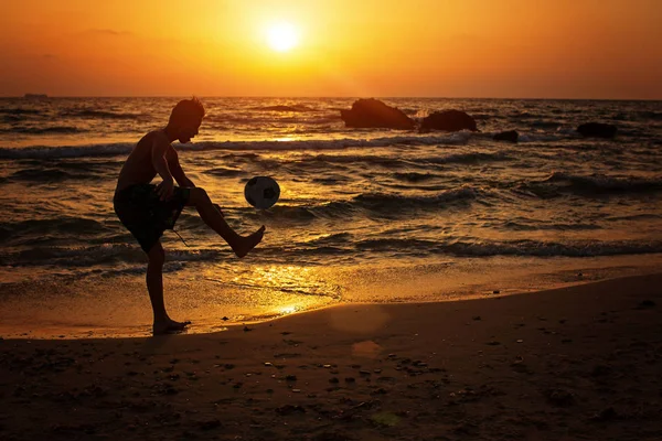 Pojke som spelar fotboll framför havet under solnedgången — Stockfoto
