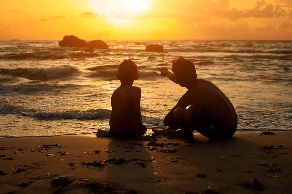 Güzel güneş battıktan sonra eğlenceli bir zevk günbatımı bakarak kum üzerinde oturan iki çocuk gün sahilde