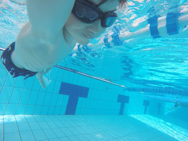 Menino está mergulhando e sorrindo debaixo d 'água em uma piscina, olhando para a câmera — Fotografia de Stock