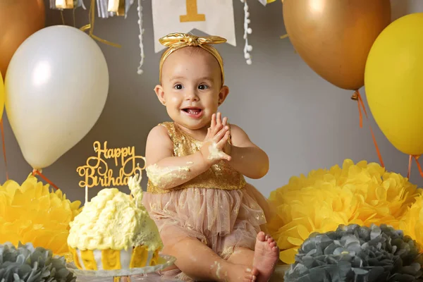 Çelenk ve topları bayraklarıyla gri bir arka plan üzerinde oturan sevimli güzel bebek. Yaşamın ilk yıl kutluyor