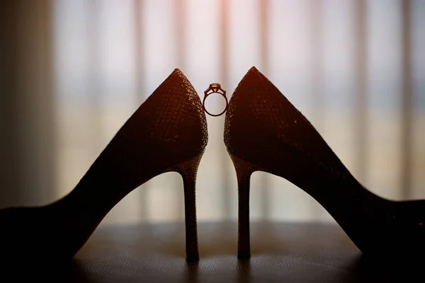 Свадебные кольца стоят перед бутылкой парфюма между шикарными туфлями белой женщины — стоковое фото