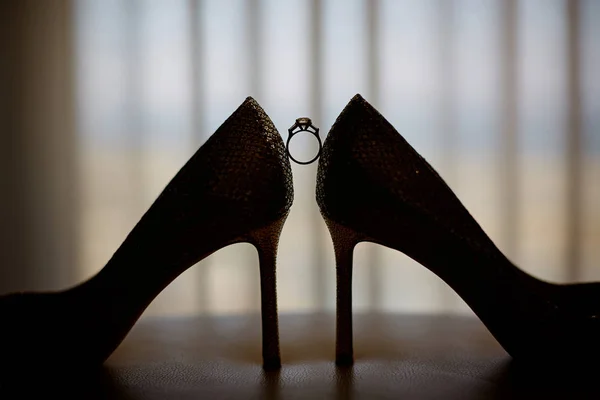 Предложение о браке. Золотые обручальные кольца и обручальное кольцо возле роскошных свадебных туфель на высоких каблуках. Лучший вид для невесты в день свадьбы — стоковое фото
