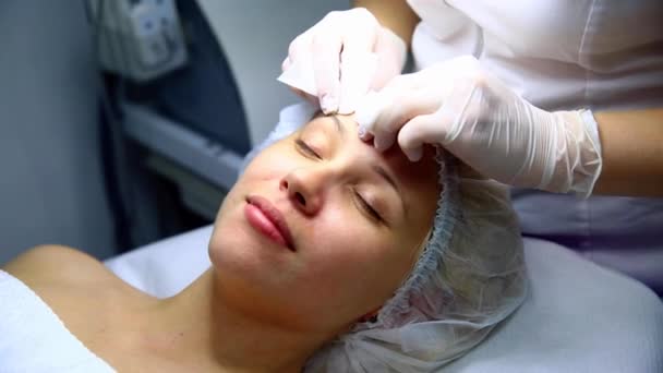 Cosmetologist limpeza mulher caucasiana rosto com esponjas. Paciente no sofá com os olhos fechados — Vídeo de Stock