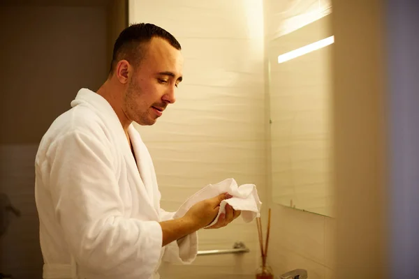 スキンケア。浴室で上半身裸で立っている間タオルで彼の滑らかな肌を拭き、彼の顔に触れるハンサムな男の肖像 — ストック写真
