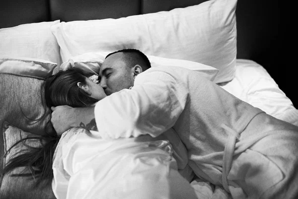 Casal romântico jovem relaxante e beijando na cama. Menina bonita e homem morena. Foto em preto e branco . — Fotografia de Stock