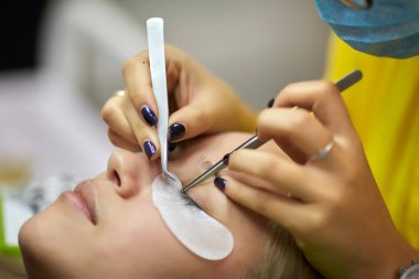 Salonda çalışma ve profesyonel yordamı kirpik uzatma için genç sarışın yapıyor kırpma kadın 