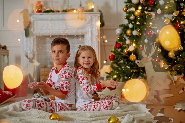 Crianças pequenas riem perto da árvore de Natal atrás das portas verdes e seguram em suas mãos não neve amanhecendo — Fotografia de Stock