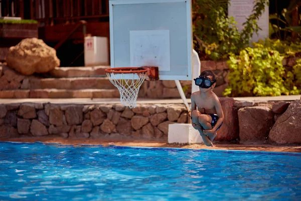 Niño caucásico divertirse haciendo salto fantástico en la piscina en el complejo. Sus brazos y piernas están bien abiertos . — Foto de Stock