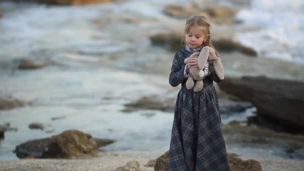 Bebé chica en vestido celebración de conejito juguete en la naturaleza, cámara lenta completa hd — Vídeo de stock