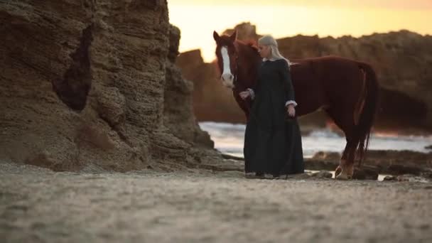 Wanita memimpin kuda saat matahari terbenam di sepanjang pantai dalam kostum bersejarah abad ke-19 — Stok Video