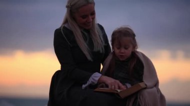 Güneş ışığı, ağır çekim Full Hd kayalık sahil üzerinde zarif elbise okuma kitabı ile küçük kız kadın yan görünüm