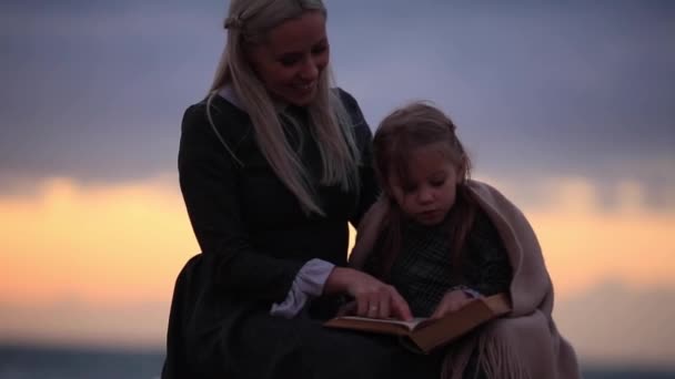 Mujer con niña leyendo libro en la orilla del mar. Cámara lenta Full HD — Vídeos de Stock