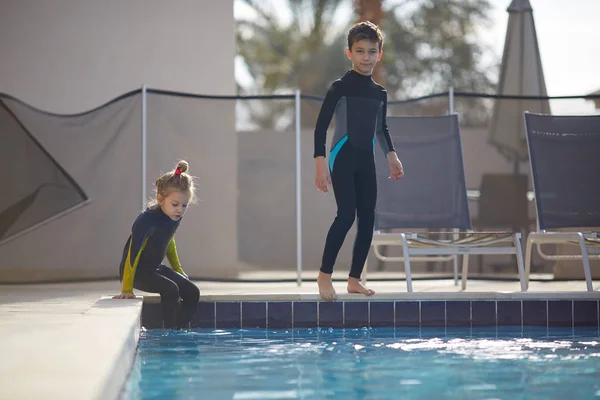 girl and boy get ready to jump into a cold pool in surfing suits