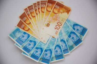 Beyaz arka plan üzerinde bir kağıt klibi yığınındaki yeni İsrail sheqalim.