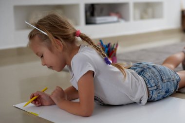 Küçük kız halının üzerinde yalan çizer