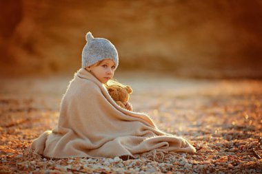 Güneş ışığı plajda otururken oyuncak ile sıcak şal şapka sarılma içinde küçük kız yan görünüm