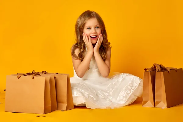 Little surprised girl holds bags on yellow background Stock Photo