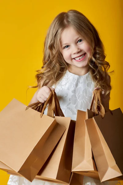 Ohromil atraktivní dítě v šatech, držící nákupní tašky na žluté — Stock fotografie