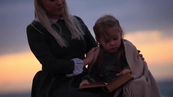 Mujer con niña leyendo libro en la orilla del mar. Cámara lenta Full HD — Vídeos de Stock