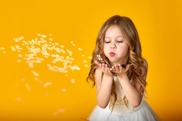 Retrato de una niña feliz soplando confeti en un color —  Fotos de Stock