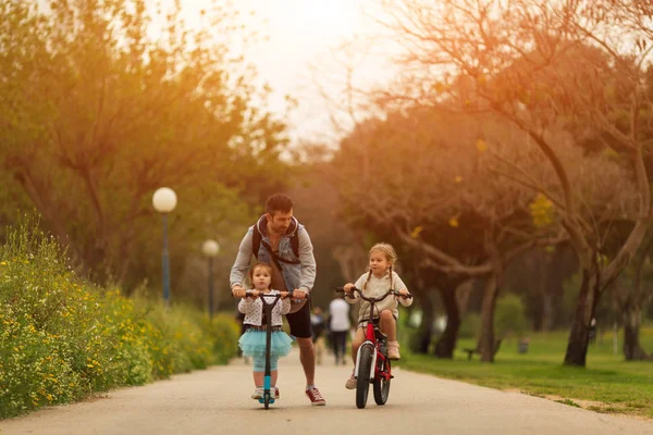 Sport attivo padre di famiglia in scooter con bambini all'aperto, bambina in bicicletta — Foto Stock