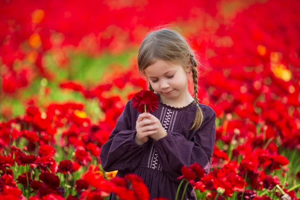 Roztomilá mladá dívka s květinou v ruce proti pozadí červených květů — Stock fotografie
