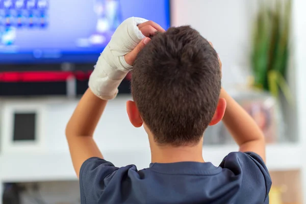 Анонимный мальчик со сломанной рукой смотрит телевизор — стоковое фото