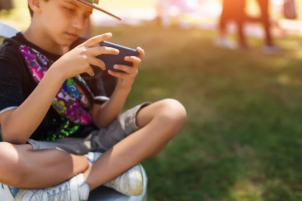 Маленький мальчик играет в мобильные игры на смартфоне в парке — стоковое фото