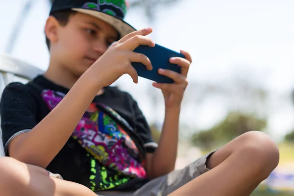 Genç çocuk parkta tek başına akıllı telefonla oynuyor. — Stok fotoğraf