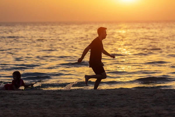 Far och unge leker på stranden vid solnedgången. Begreppet vänlig familj — Stockfoto