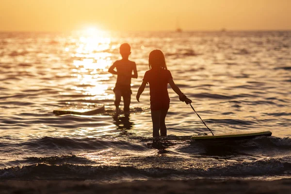 Las siluetas de los niños durante las vacaciones de verano. relajarse en el mar en la hora dorada —  Fotos de Stock