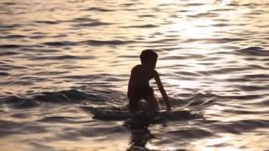 Gün batımının mükemmel arka planında sörf tahtası ile denizde yüzen bir çocuğun silueti 