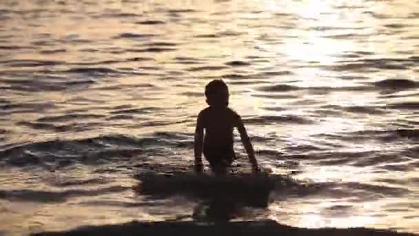 Silueta de un niño flotando en el mar con una tabla de surf en el excelente atardecer de fondo — Vídeos de Stock