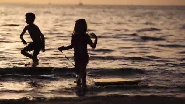 Glückliche Kinder, die am Strand bei Sonnenuntergang spielen. Konzept des Sommerurlaubs, freundliche Familie — Stockvideo