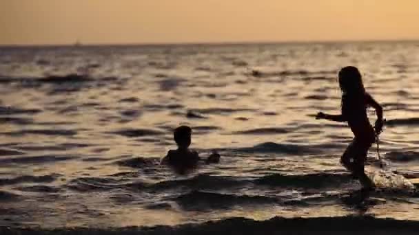 Silhuetter av barn bada i den gyllene solnedgången i sommarlovet till sjöss — Stockvideo