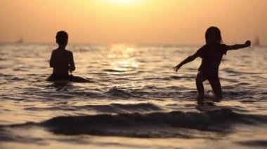 Güneş parlamasında deniz suyunda oynayan çocuklar, denizde oynayan tanınmayan çocuklar silueti