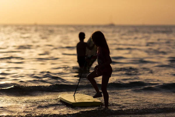 Silueta de una chica corriendo en una playa con una pequeña tabla de surf en sus manos —  Fotos de Stock