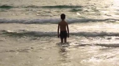 Çocuk Çocuk yaz günbatımı plajda dalgalar oynarken, Çocuk deniz dalgaları izlerken ve eğlenmek
