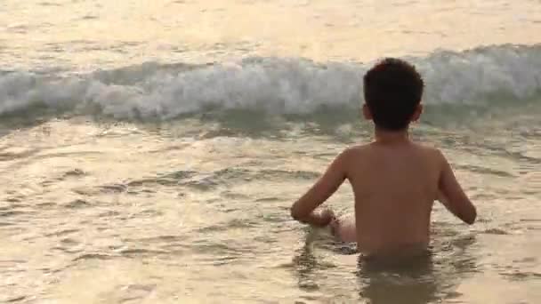 Menino alegre feliz se divertindo e jogando para o mar. Menino brincando na praia ao pôr do sol — Vídeo de Stock