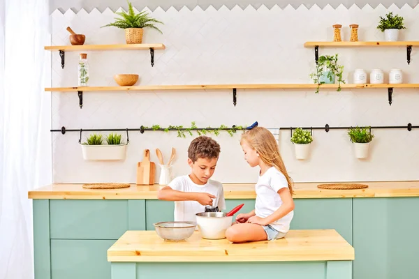 Little Friends Are Making A Cake Together At A Kitchen Against A White Wall With Shelves On It