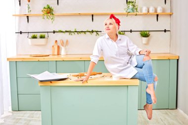 beyaz gömlek kırmızı bir kafa bandı ile genç sarışın pişirme için hamur ile mutfak masasına oturur