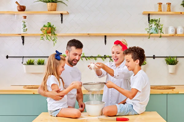 Familia feliz en la cocina.Padre e hijos preparando galletas en la cocina. Madre vertiendo harina — Foto de Stock
