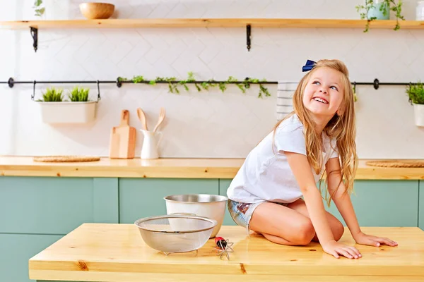 Веселая маленькая девочка сидит на кухонном столе — стоковое фото