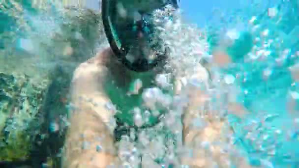 Gezicht jonge man in snorkelen masker en snorkel terwijl onderwater zwemmen in blauwe zee. — Stockvideo